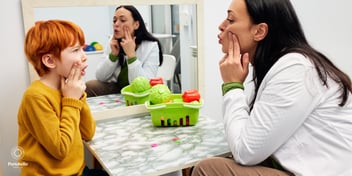 a speech and language therapist holding her face and a child copying her to make a sound