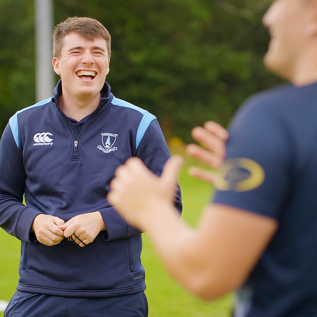 An athlete and colleague smile on the training pitch