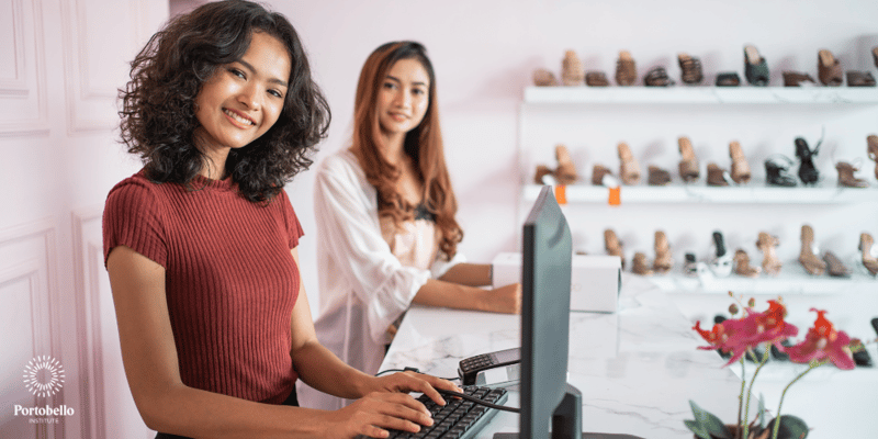 Two women looking at the camera while working on a computer in a retail setting