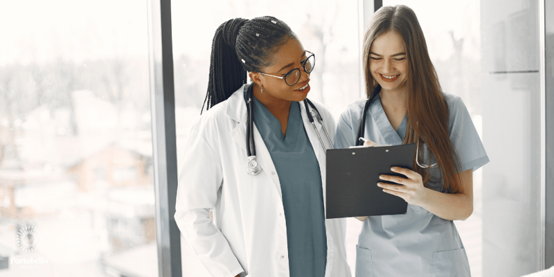 A doctor and a nurse talking and holding a clipboard in front of a large glass window