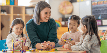 smiling preschool teacher with three young girls at a table