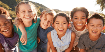 a group of children linking arms smiling at the camera sun shining in the background