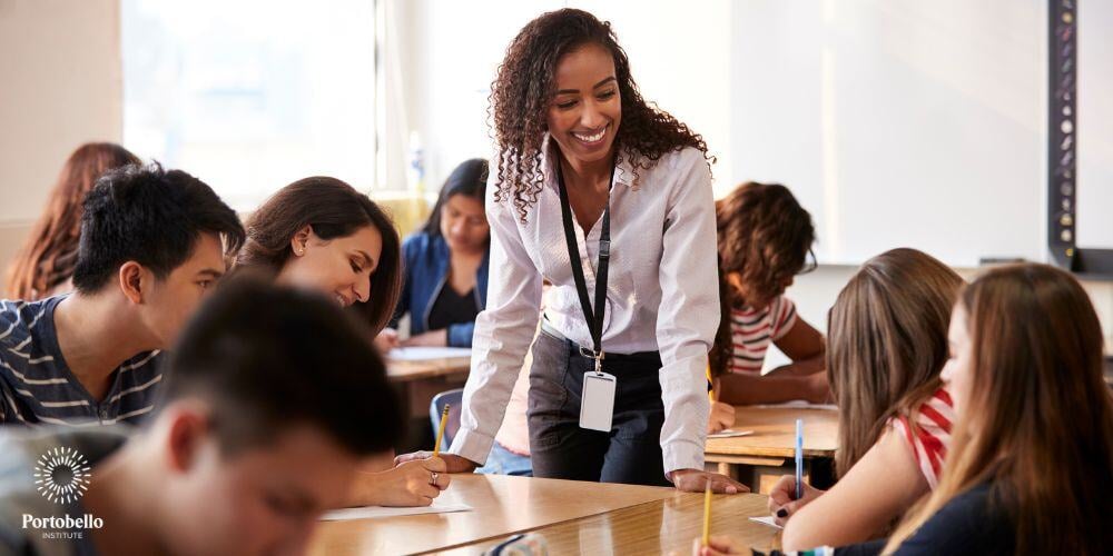 A teacher leaning over a desk surrounded by young students with their heads down working