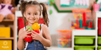 Little girl smiling at the camera in a preschool holding colourful balls