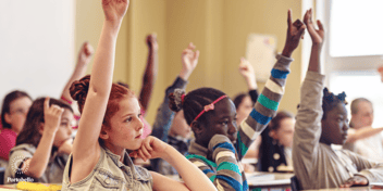 A group of young children in a classroom with their hands up