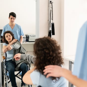 An occupational therapist helps a woman in a wheelchair get dressed