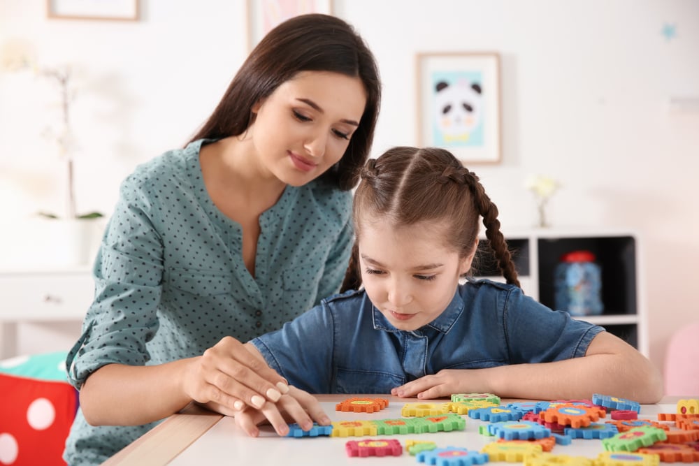 Adult woman working one to one with a young child sitting at a table