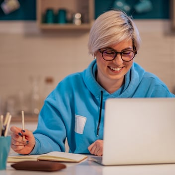 A woman studying independently at home using a laptop and notebook