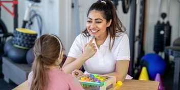 a speech and language therapist holds her finger to her mouth working with a child