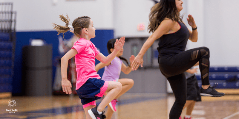 A pe teacher in mid air doing high kicks with young students