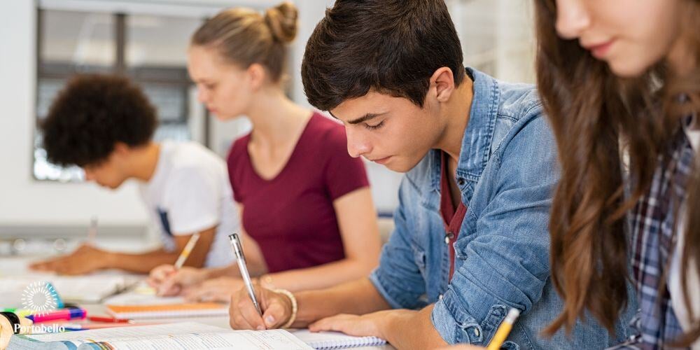 teenage students sitting in a row writing in notebooks