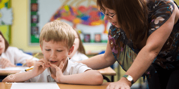 teaching assistant helping a young boy in a school classroom