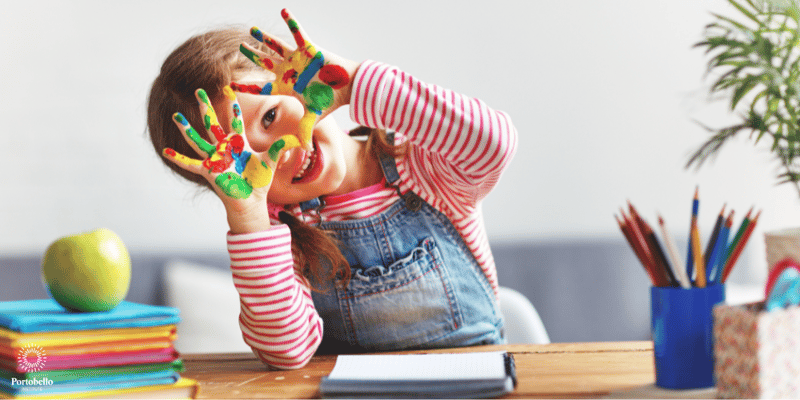 A child sitting at a desk with paint on her hands smiling 