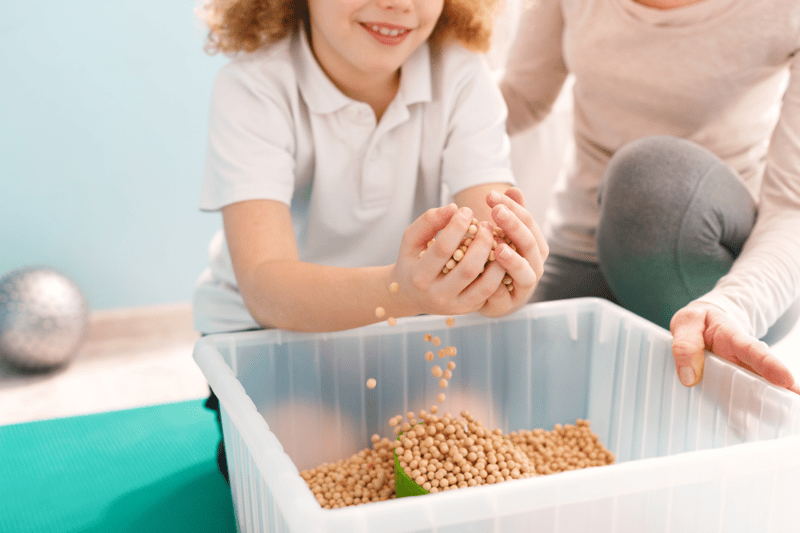 A child picking up dried beans from a plastic container and feeling them in their hands