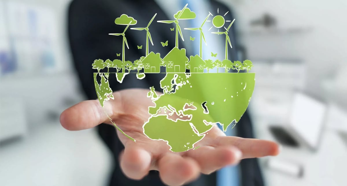 A man holds a vibrant green, stylized globe with eco-friendly symbols like wind turbines, trees, and houses rising from it, representing environmental sustainability.